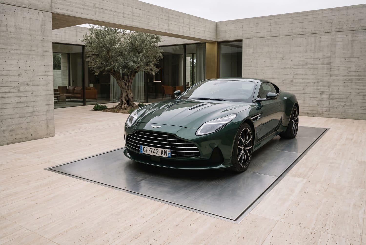 Coupé de sport à l'arrêt sur la plateforme d'un monte-voiture affleurant le dallage travertin d'une cour de villa en béton, plantée d'un olivier
