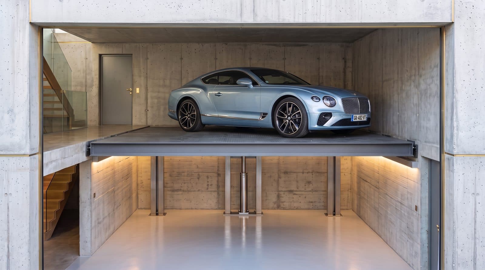 Coupé de luxe sur la plateforme d'un monte-voiture deux niveaux arrêtée au niveau haut, colonnes de guidage et niveau inférieur éclairé visibles sous le plateau