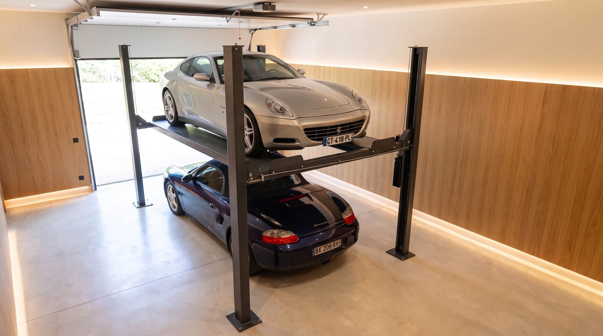 Doubleur de parking à quatre poteaux dans un garage de villa, coupé gris sur le plateau levé, cabriolet bleu garé dessous