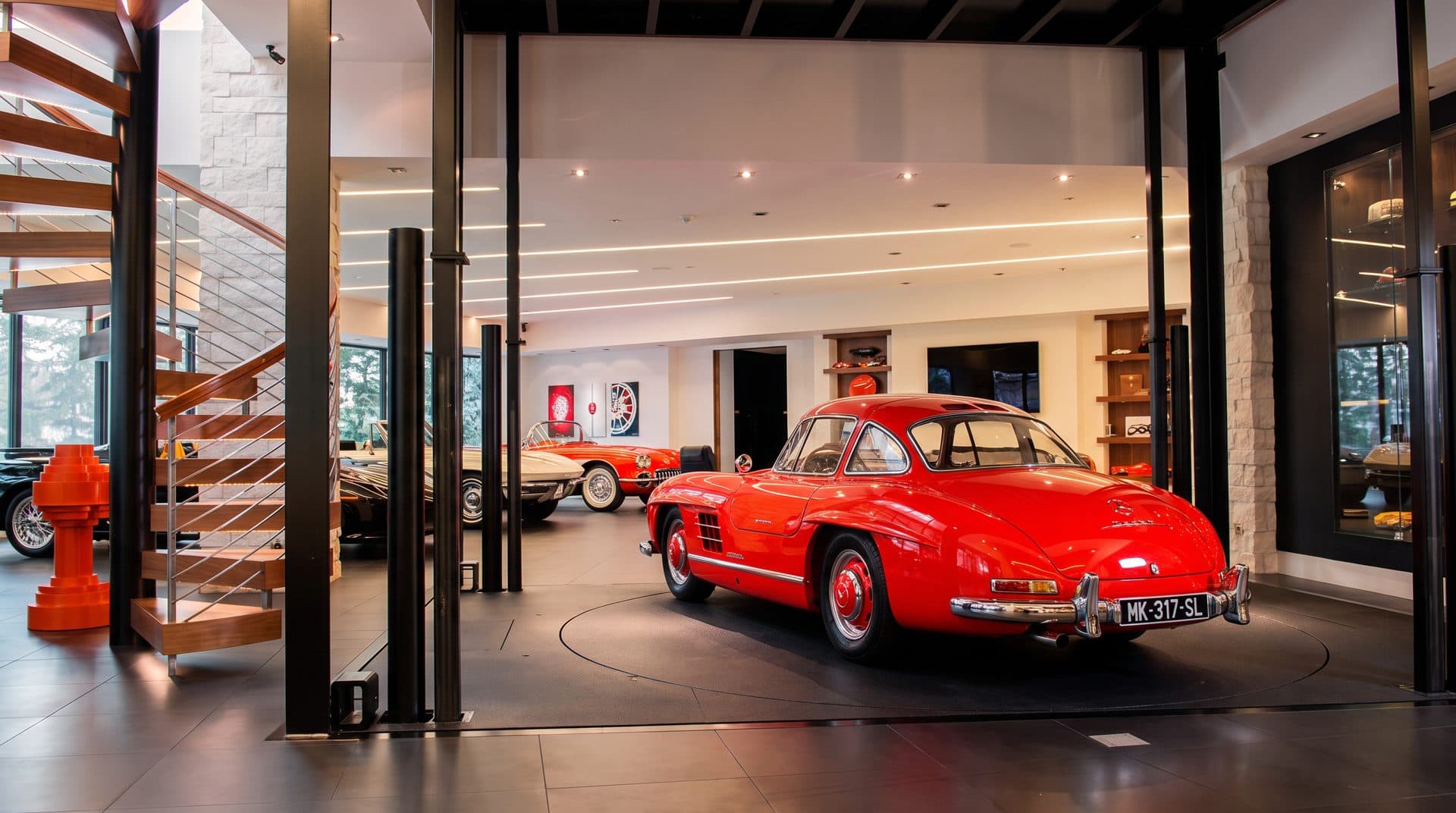 Coupé rouge ancien posé sur un plateau tournant au ras du sol, dans une galerie de collection intérieure